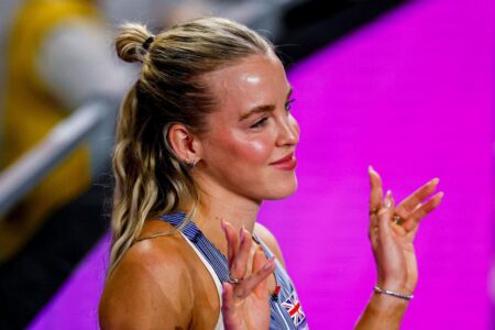 كيلي هودجكينسون تبتسم في مضمار ألعاب القوى مع شعار ملعب لندن في الخلفية.